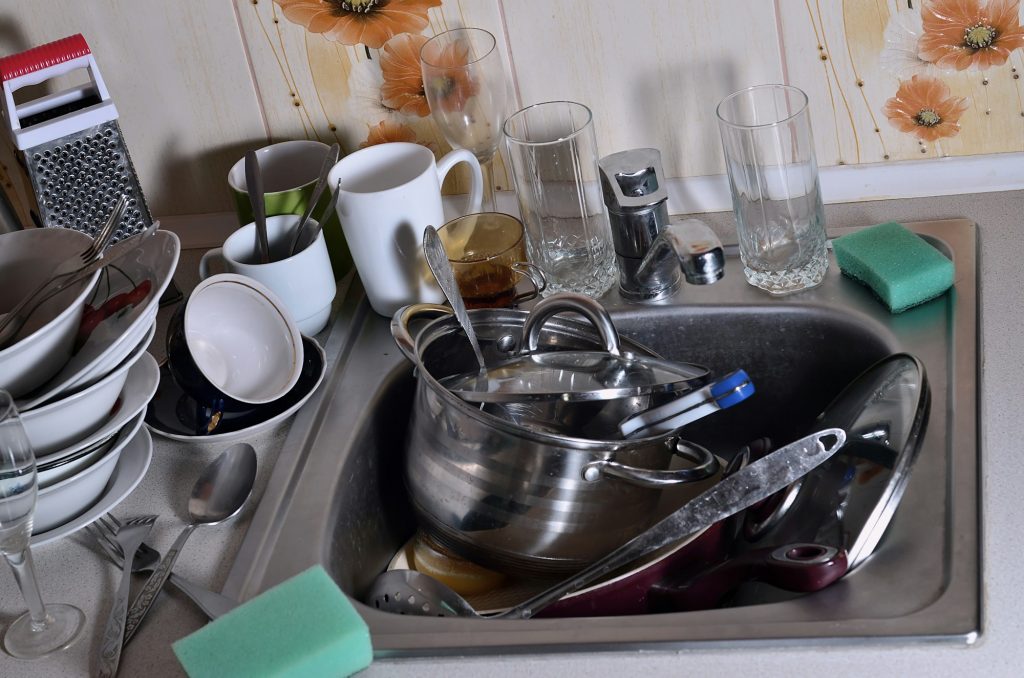 A huge pile of unwashed dishes in the kitchen sink and on the countertop