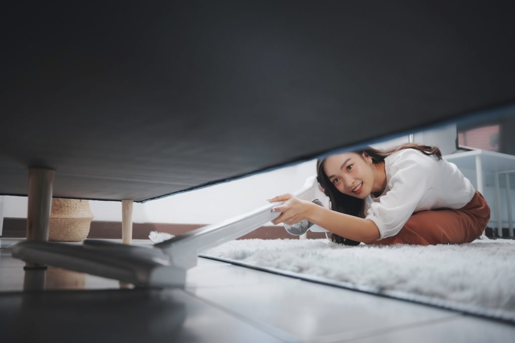 Woman using cordless vacuum cleaner cleaning under sofa in living room