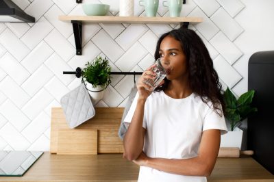 African girl stands on the kitchen and drinks water